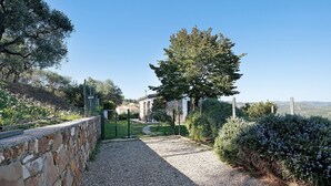 A gravel pathway leading to a stone wall, a large tree, and a building with a stone facade. - Apartment "La Casa di Lele" with Sea View, Private Garden and Wi-Fi (Costarainera)