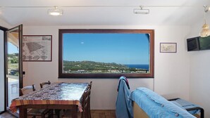 A room with a dining table, chairs, a bench, a large window with a view, and a map on the wall. - Apartment "La Casa di Lele" with Sea View, Private Garden and Wi-Fi (Costarainera)