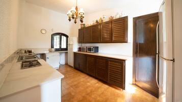 Eine Küche mit Mikrowelle, Backofen und Kühlschrank. Oberhalb der Arbeitsfläche befindet sich ein Holzschrank, an der Decke hängt eine Chandelier.
