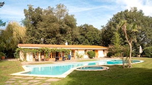 Una casa con piscina, rodeada de jardín y árboles.