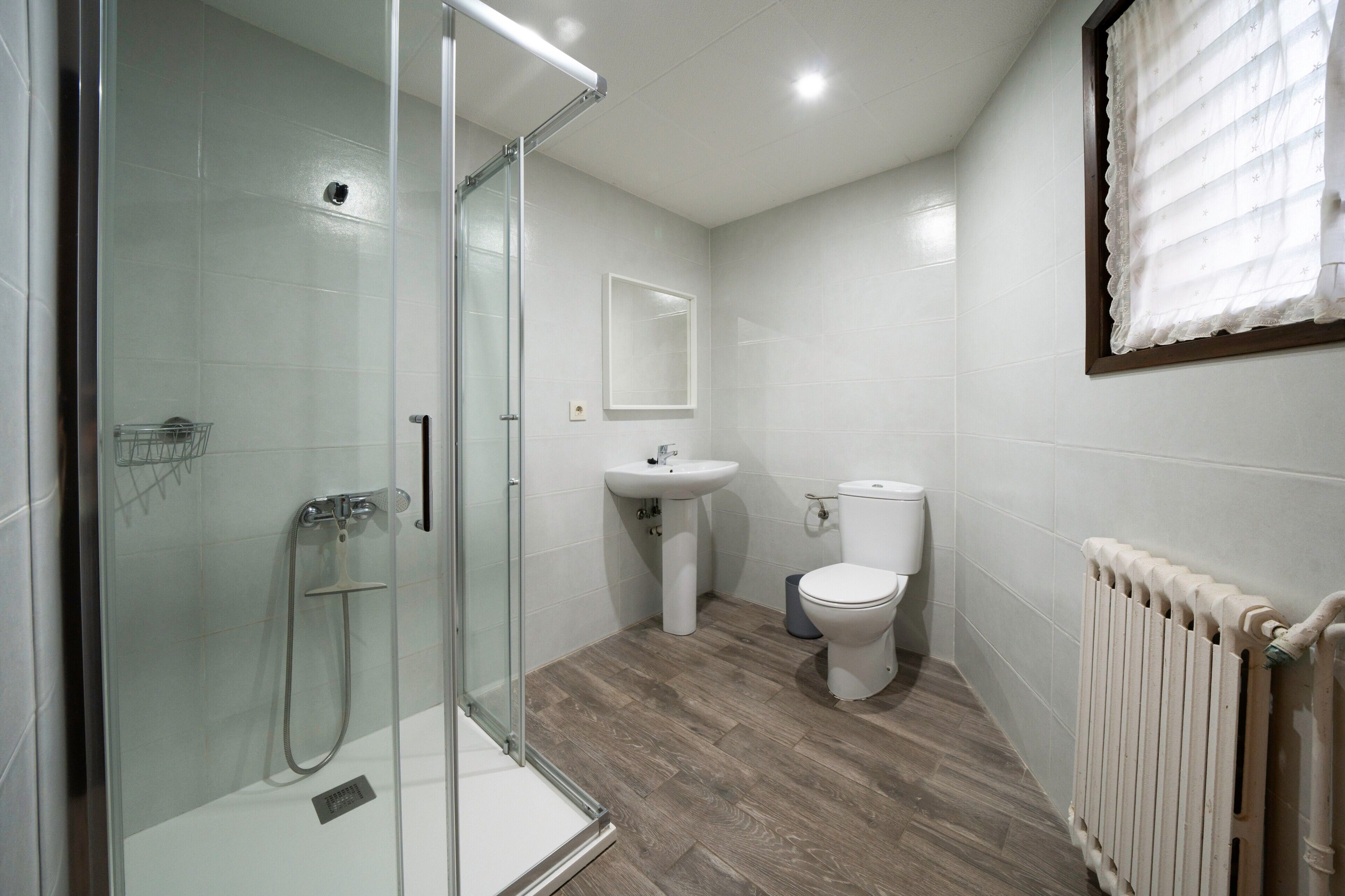 Un baño moderno con cabina de ducha de cristal, lavabo pedestal, inodoro y radiador.