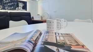Une chambre moderne avec une table blanche, deux tasses blanches ornées du logo d’Italianway, un magazine posé sur la table et un canapé noir à l’arrière-plan.