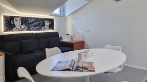 Une pièce moderne avec un canapé foncé, une table ronde blanche et une œuvre d’art accrochée au mur.