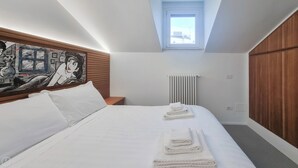 Une chambre d’hôtel moderne avec un grand lit, un tableau au mur, une fenêtre et un radiateur.