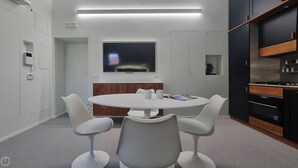 Une salle de réunion moderne dotée d’une table ronde, de chaises blanches, d’un téléviseur à écran plat et de meubles encastrés.