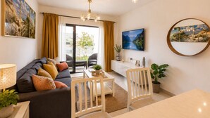 A modern living room with a sofa, dining table, chairs, a TV, and artwork on the walls.