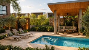 A modern outdoor pool area with lounge chairs, a covered seating area, and lush greenery.