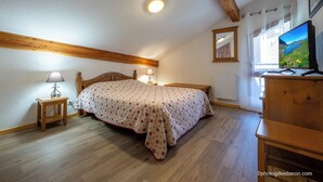 Ein Schlafzimmer mit einem Bett, Nachttischlampen, einer Holzkommode, einem Fernseher und einem Fenster mit Seeblick.