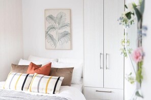 A bedroom with a bed, pillows, a framed botanical print on the wall, and a wardrobe.