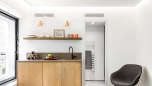 A compact kitchen with wooden cabinets, a sink, and a countertop with various items. There is a chair and a door leading to another room.