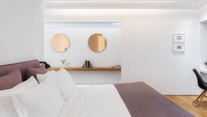 Een moderne hotelkamer met een groot bed, een houten nachtkastje, een ronde spiegel en een klein plankje met boeken en decoratieve objecten.