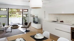 A modern kitchen with white cabinets, a dining area with a wooden table, and a TV on a white cabinet. - Family Maisonette, Urban Stripes Athens (Athens)
