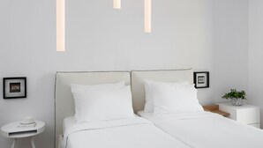 A modern bedroom with a large bed, white bedding, a small bedside table with a book and a framed picture, and a nightstand with a plant. - Family Maisonette, Urban Stripes Athens (Athens)