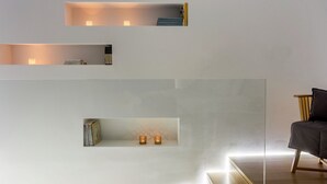 A minimalist room with built-in shelves containing books and decorative items, a wooden chair, and a glass table. - Family Maisonette, Urban Stripes Athens (Athens)