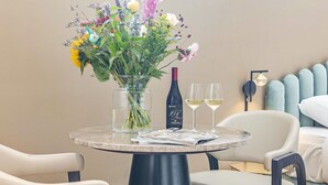Una mesa redonda con un jarrón de flores, una botella de vino y dos copas sobre una mesa de habitación de hotel.