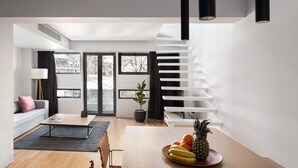 A modern living space with a staircase, a dining area with fruits, a sofa, and a large window.