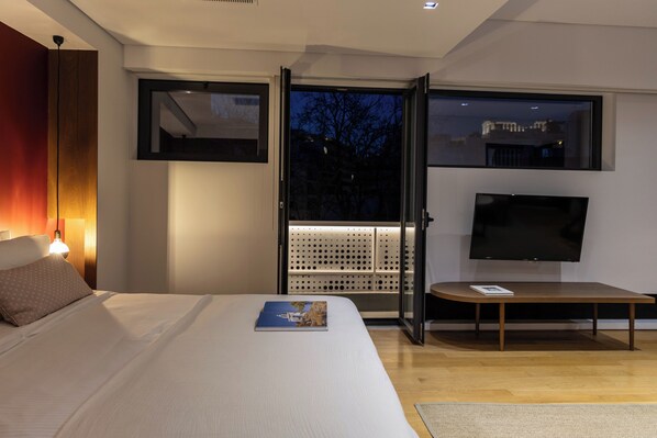 A modern bedroom with a bed, a TV, a sliding door to a balcony, and a nightstand with a lamp.
