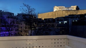 En balkon med et bord og en stol, der kigger ud over en historisk bygning med søjler, under en stjerneklar nattehimmel.