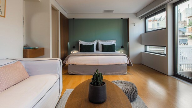 Et moderne hotelværelse med seng, sofa, sofabord med en kaktus og et stort vindue med udsigt over byen.