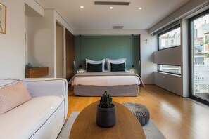 A modern hotel room with a bed, a sofa, a coffee table with a cactus, and a large window offering a city view. - Acropolis Suite II, Urban Stripes Athens (Athens)