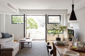 A modern apartment with a dining area, a sofa, and a large window offering a view of the city. - Acropolis Maisonette, Urban Stripes Athens (Athens)