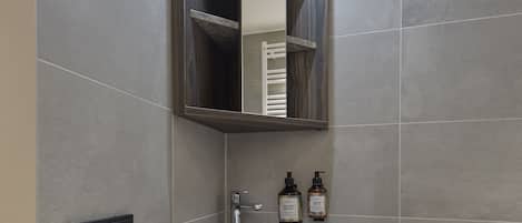 Un baño moderno con encimera de mármol, lavamanos, espejo y estante con toallas.