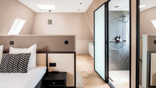 A modern hotel room with a bed, bedside table, and a glass-enclosed shower area. - Breathe Boutique hotel Leiden (Leiden)