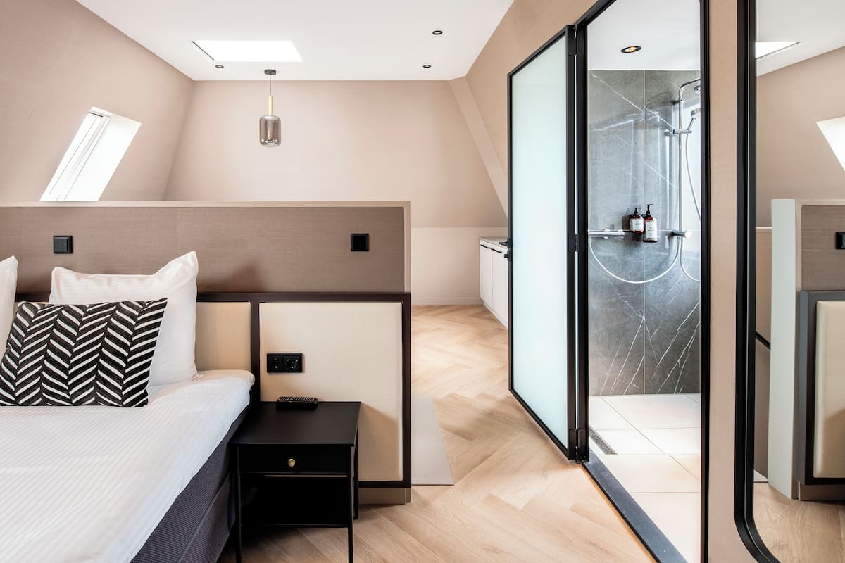 A modern hotel room with a bed, bedside table, and a glass-enclosed shower area.