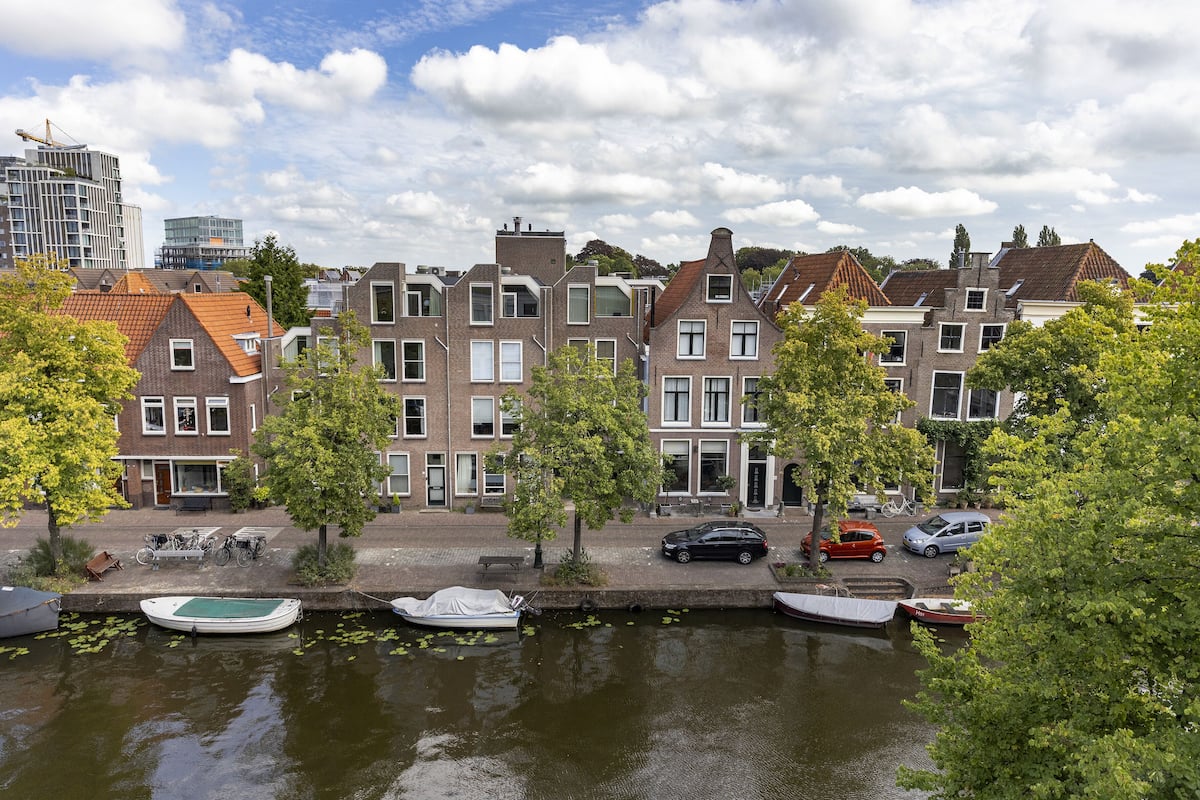 A canal with boats, a row of traditional houses, and a modern building in the background.