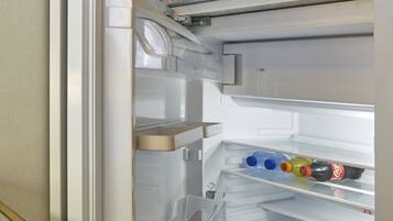 An open refrigerator with clear shelves, a water dispenser, and a coffee maker on the top shelf.