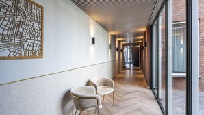 A hallway with a wooden floor, two upholstered chairs, a wall-mounted map, and a glass door leading to an outdoor area. - Breathe Boutique hotel Leiden (Leiden)