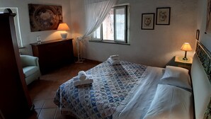 Un dormitorio con cama, mesita de noche, ventana con cortinas, lámpara y un cuadro en la pared.