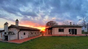 Entorno rural con dos edificios, uno con un campanario y otro de techo plano, al atardecer.