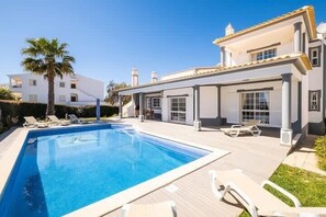 Une villa moderne dotée d’une piscine, de chaises longues et d’un jardin bien entretenu.