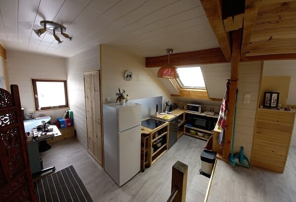 A compact kitchen with a refrigerator, microwave, and wooden cabinets. There's a window providing natural light and a skylight above the sink.