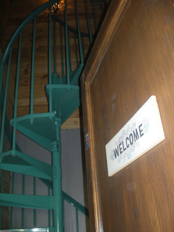 Una escalera de caracol con un letrero de 'WELCOME' en una puerta de madera.