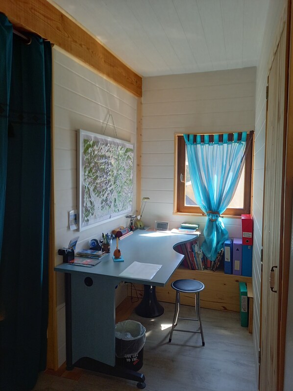 Una habitación pequeña y acogedora con escritorio, silla y ventana con cortinas azules.