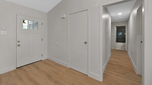 A hallway with wooden flooring, white walls, and a door leading to a bathroom. - Fire Pit ☀️ Grill - Hammock - King Bed 🏡 1 Story Home (The Woodlands)