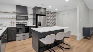 A modern kitchen with a central island, black cabinetry, stainless steel appliances, and a patterned backsplash. - Fire Pit ☀️ Grill - Hammock - King Bed 🏡 1 Story Home (The Woodlands)