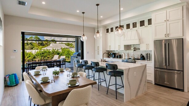 Una cocina moderna con armarios blancos, un refrigerador de acero inoxidable y un comedor con una mesa dispuesta para seis personas.