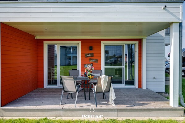 Une terrasse couverte avec une table et des chaises, un petit jardin et une enseigne indiquant « Port54 ».