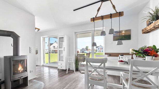 Cozinha moderna com lareira a lenha, armários brancos e uma janela grande com vista para uma área residencial.