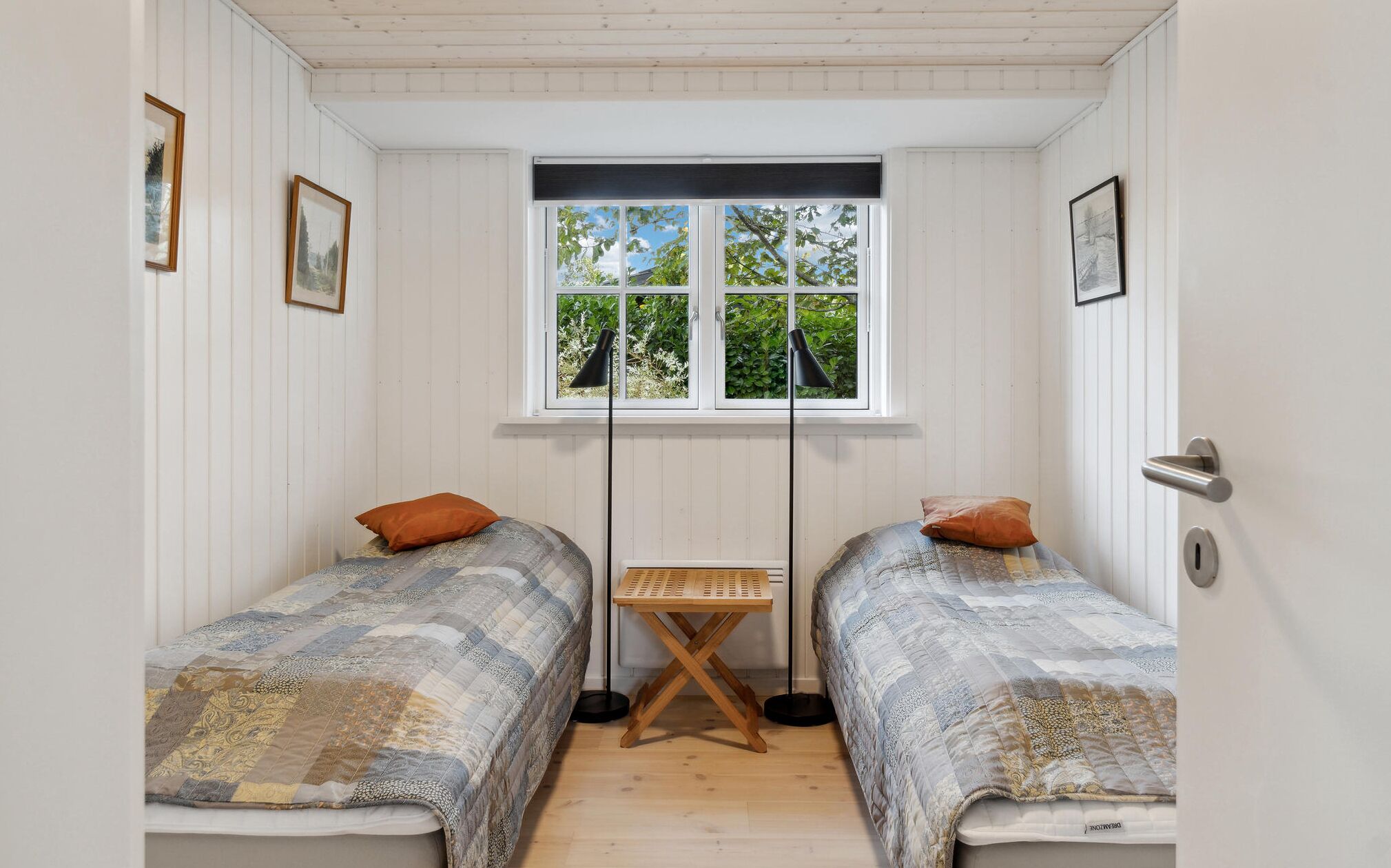 Ein kleines Zimmer mit zwei Einzelbetten, einem Fenster mit Blick ins Grüne und einem kleinen Tisch in der Mitte.