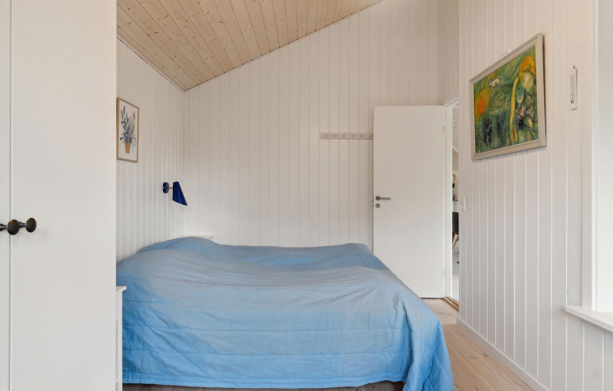A bedroom with a bed, a door, a wall-mounted lamp, and a painting.