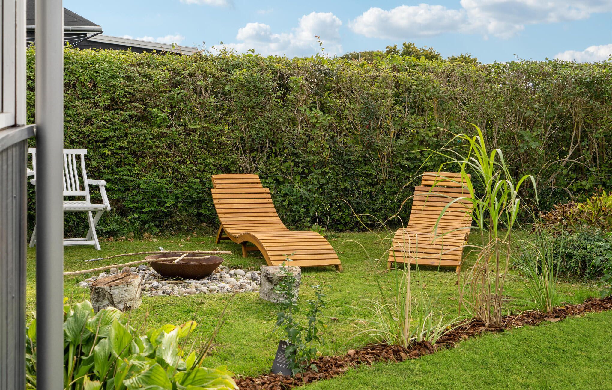 Un jardin avec deux fauteuils de jardin en bois, une chaise blanche et un foyer.