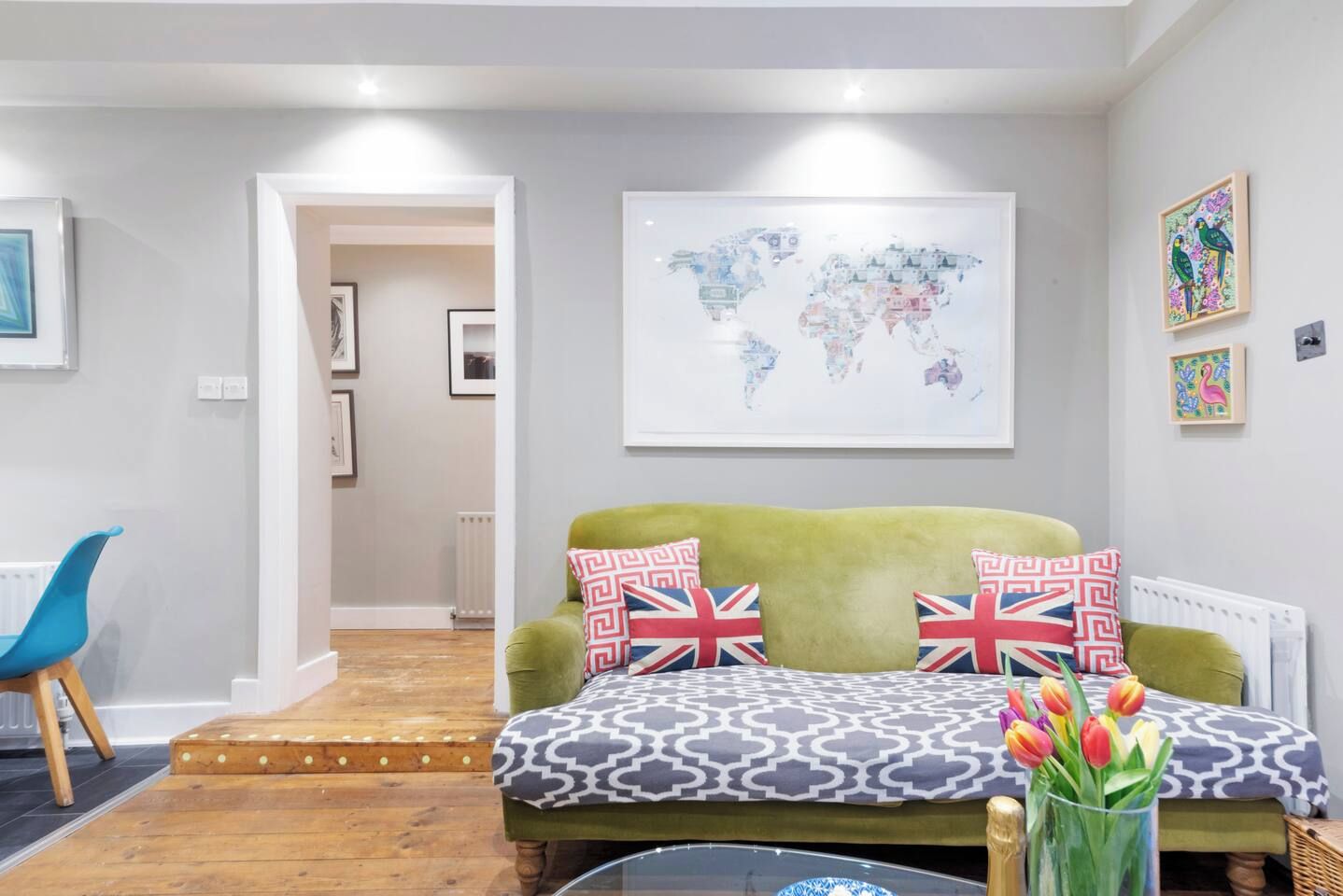 A cozy living room with a green sofa, a world map on the wall, and a small table with tulips.