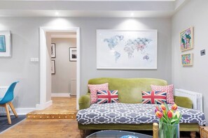 A cozy living room with a green sofa, a world map on the wall, and a small table with tulips.