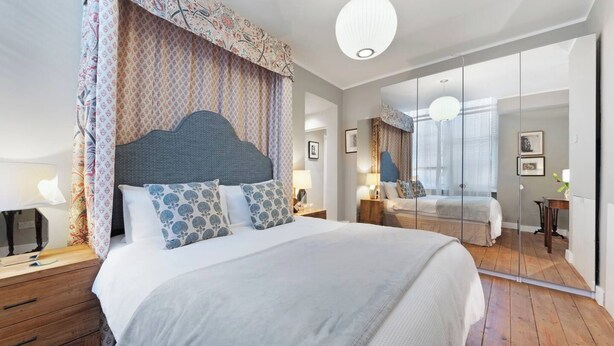 Un dormitorio moderno con una cama grande, una mesita de noche, un espejo y vistas a la habitación contigua.