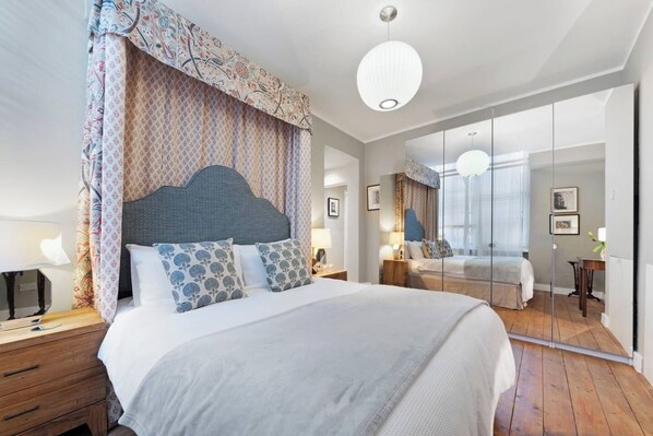 A modern bedroom with a large bed, a bedside table, a mirror, and a view of the adjacent room.