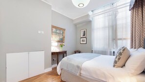 Un dormitorio con cama, mesita de noche, lámpara y ventana con cortinas.
